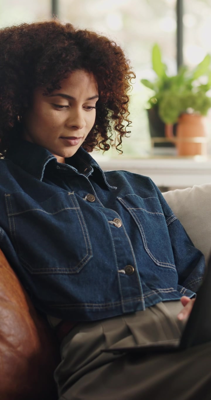 Ung kvinde bruger tablet, mens hun sidder på en læder-sofa