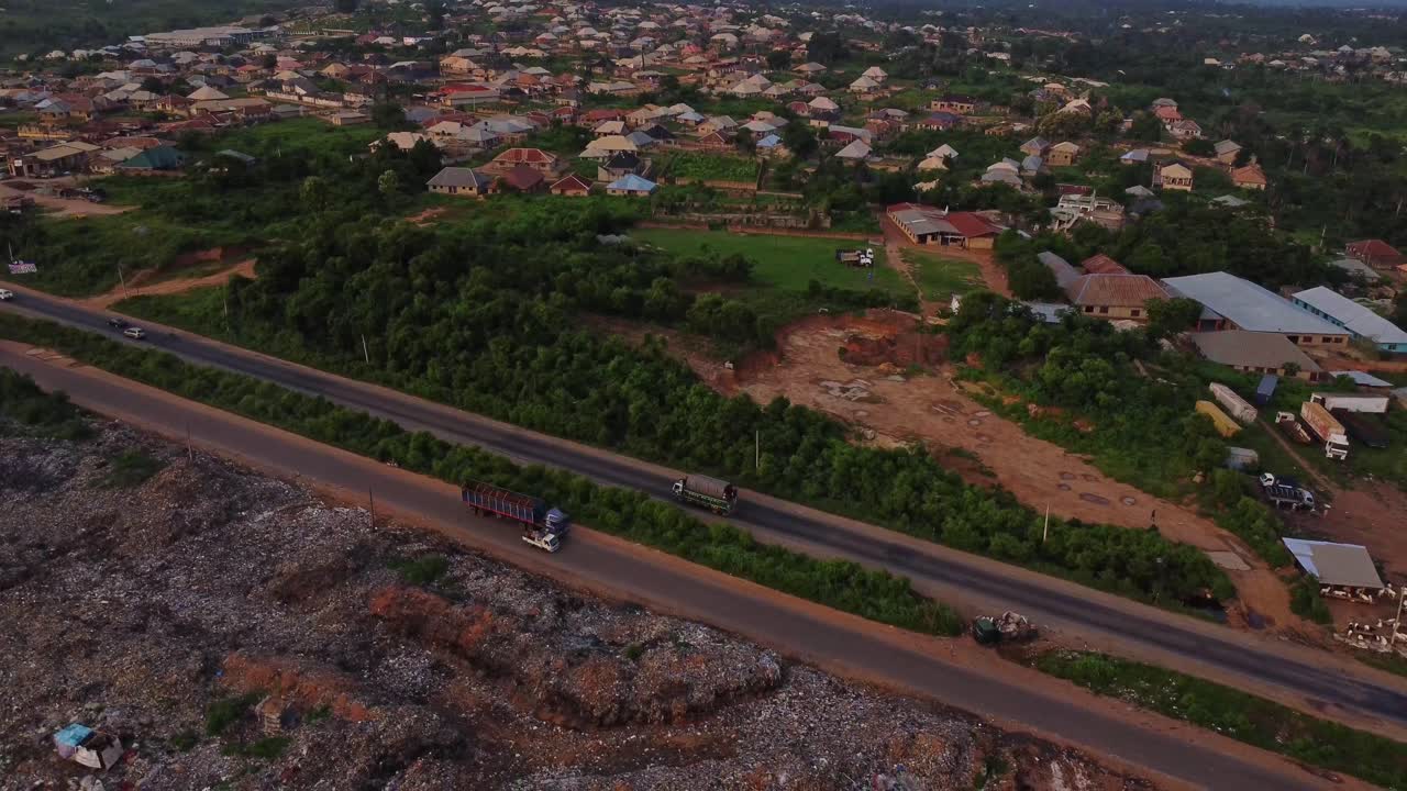 Aerial view of a busy highway next to a open air landfill in Nigeria, Africa. A small town can be seen in the background