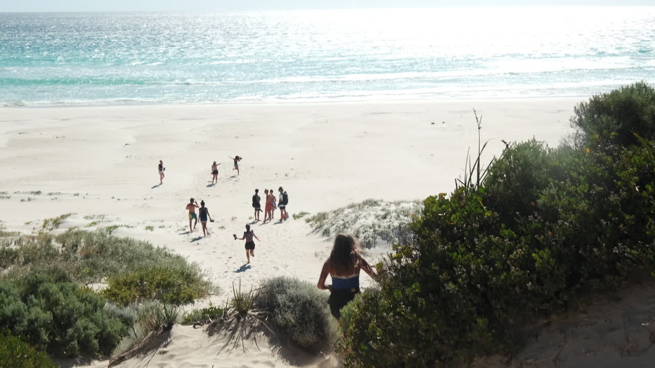 captura trasera de una linda joven corriendo cuesta abajo hacia la playa dorada, australia