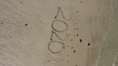 aerial camera looking straight down and turning showing twenty twenty written in the sand on a beach