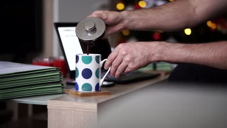 caucasian man pouring coffee into a mug in his home office during christmas time, 4k