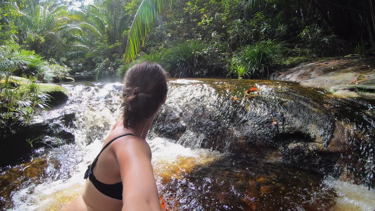 Authentic young woman in a bikini filming herself in the jungle as she is enjoying a natural river in the tropical rain forest in Borneo, Malaysia. Adventure, travel and nature concept