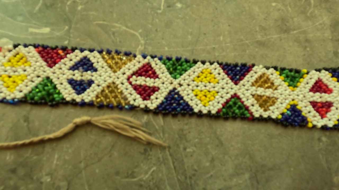 Ornamento tradizionale Amazigh con perline dal Marocco, caratterizzato da motivi geometrici a diamante e colori vivaci, che mostra simbolismo culturale, artigianato e uso decorativo nell'abbigliamento tradizionale.