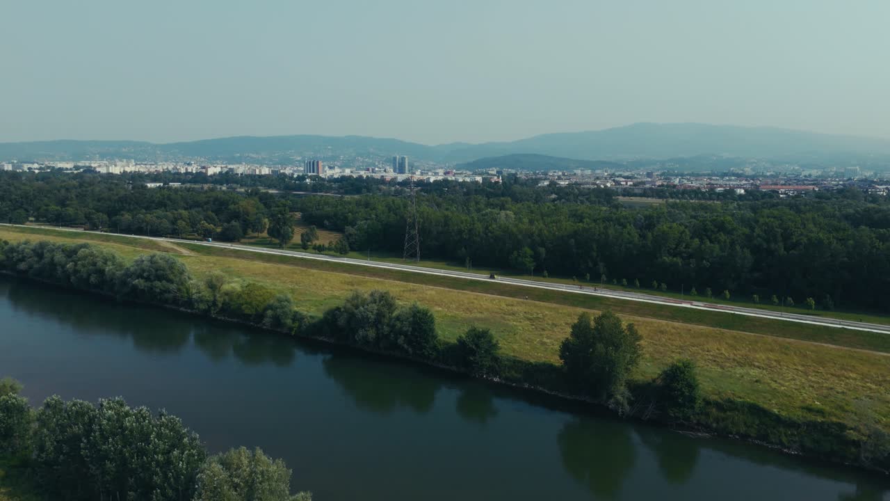 aerial - Sava River with forest edge, grasslands, and distant Zagreb city buildings