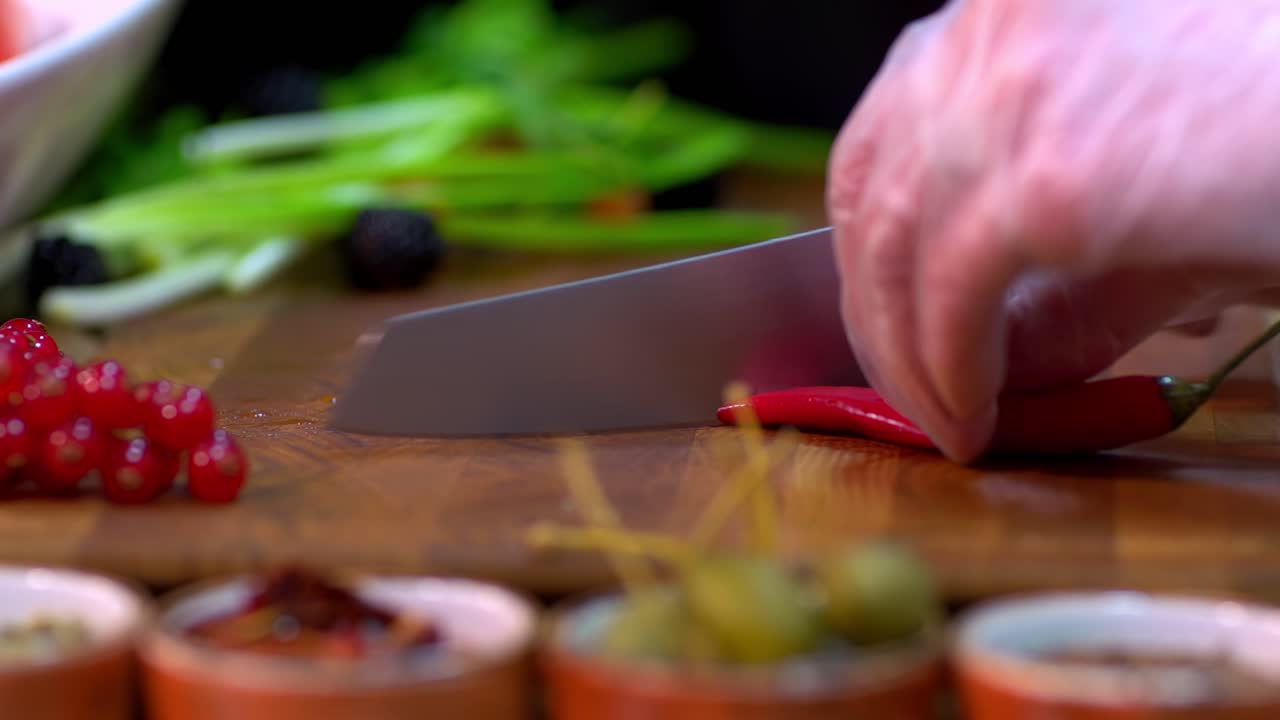 Slicing fresh red chili pepper on wooden cutting board for spicy cooking preparation, focus pull