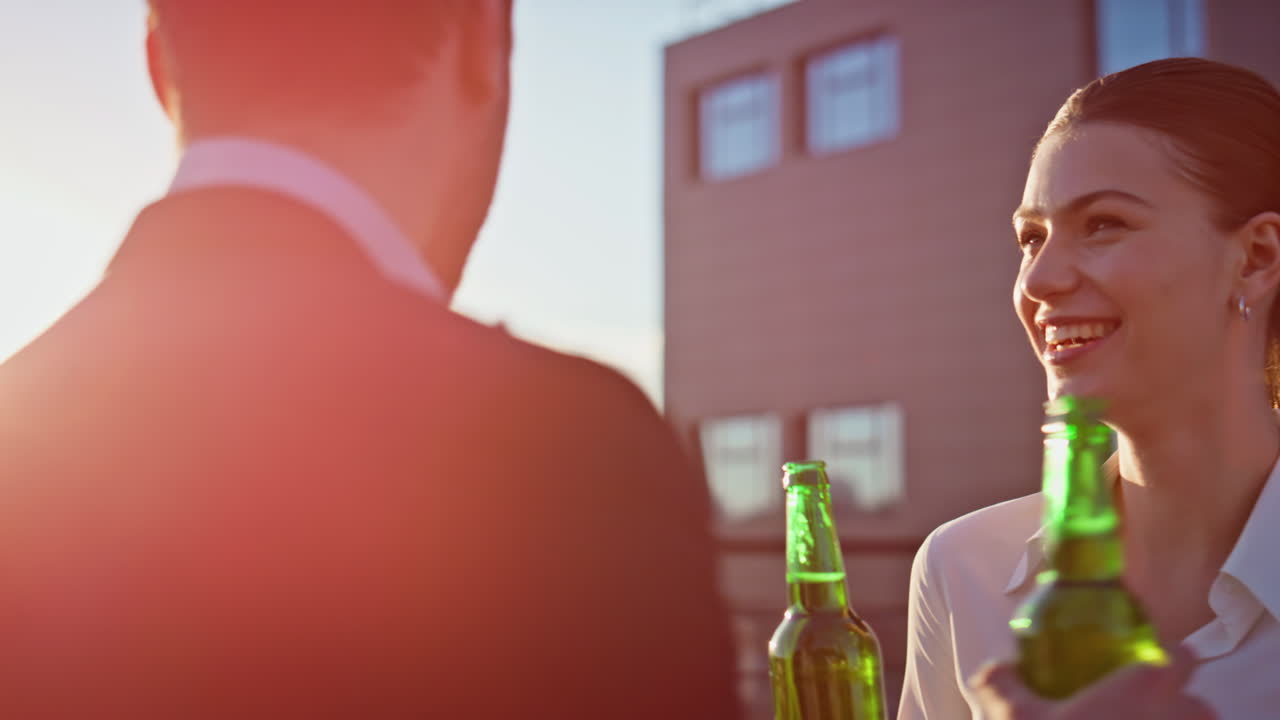 Cheerful colleagues drinking beer on sunset rooftop closeup. Relaxed friends
