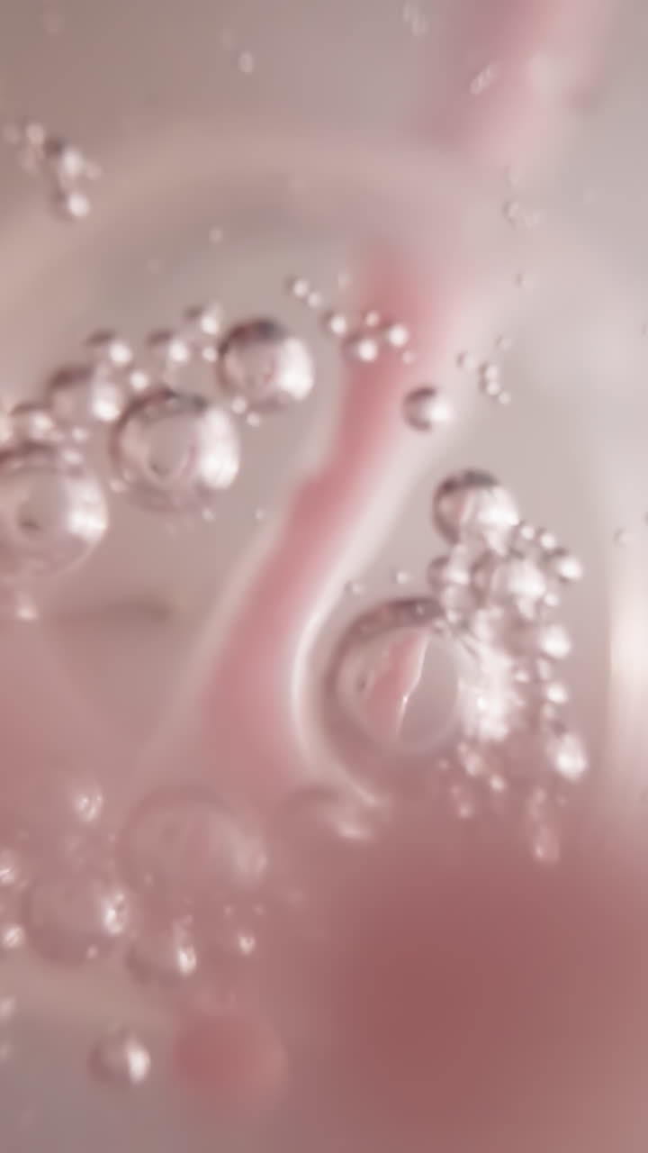 Woman dissolves raspberry balls for sweet berry taste. Candies fall into clean water with gas bubbles in plastic bottle macro low angle shot