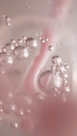 woman dissolves raspberry balls for sweet berry taste. candies fall into clean water with gas bubbles in plastic bottle macro low angle shot