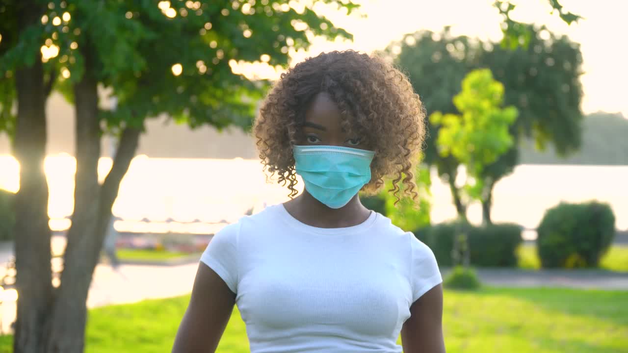 African american girl in medical mask looking at the camera in park