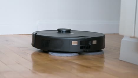 an autonomous robot vacuum cleaner spins, mops, and cleans a hardwood floor in a home living room