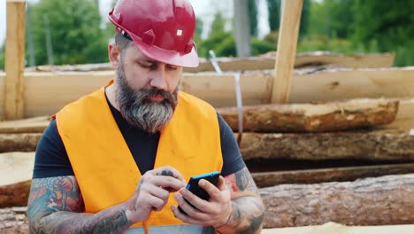 a bearded builder in a helmet uses a smartphone