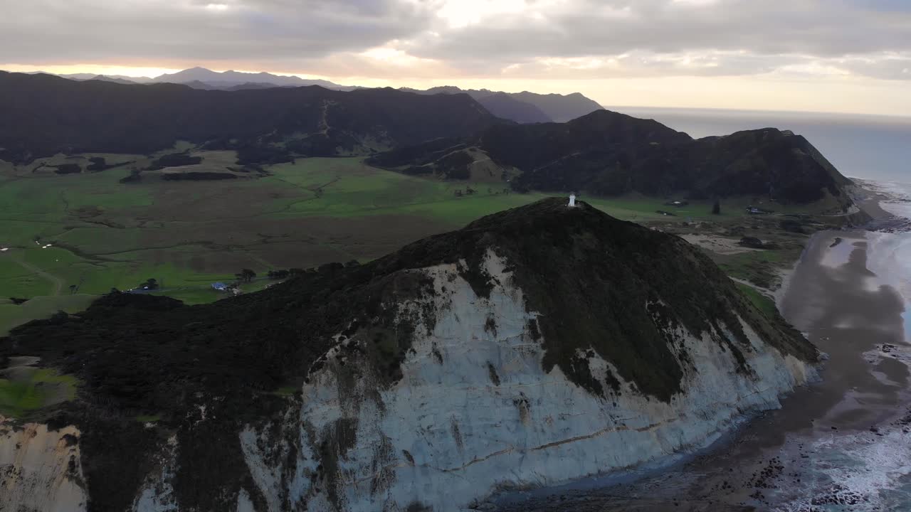 faro blanco en la cima de la montaña en el cabo este de nueva zelanda - toma aérea