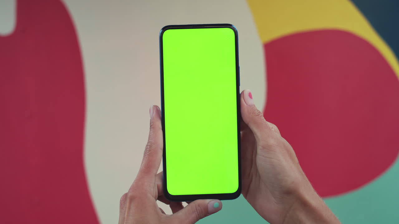 Hands Holding Smartphone with Green Screen Against a Colorful Background