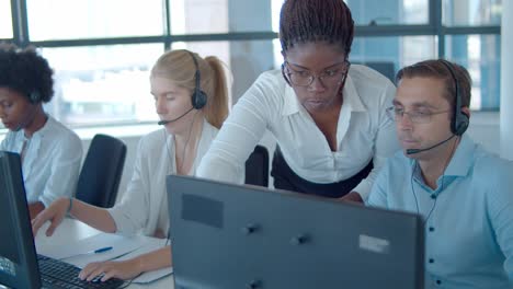 gerente afroamericano serio que ayuda a los trabajadores del centro de llamadas