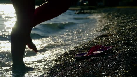 person walking on the beach at sunset during summer vacation holidays slow-motion, closeup of legs and feet with slippers in the sea water, 4k video