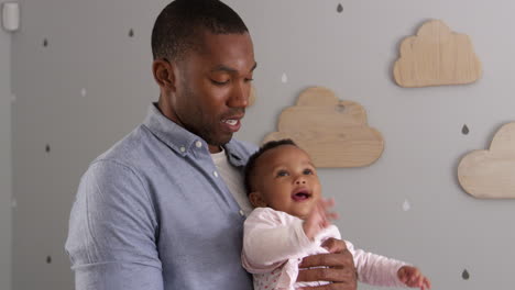 portrait of father holding baby daughter in nursery