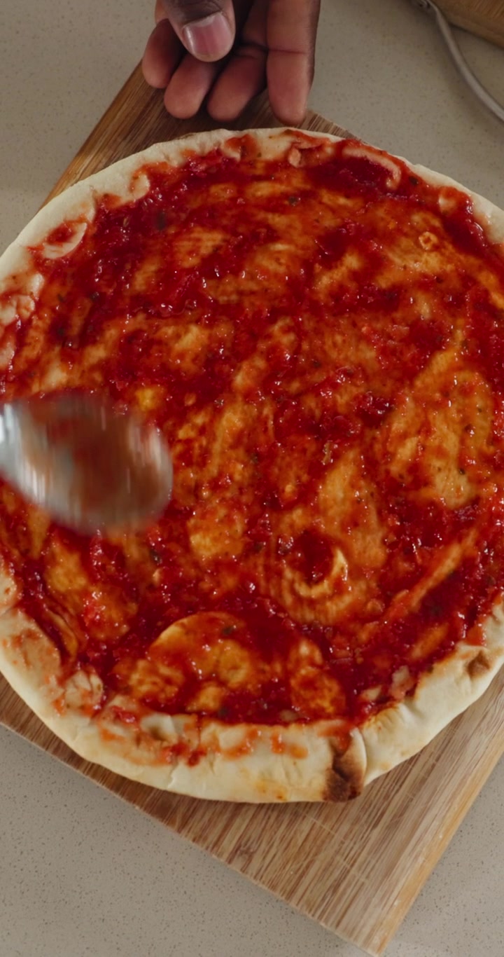 Il cuoco che spruzza la salsa di pomodoro sulla pasta della pizza