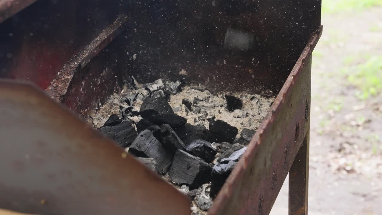 Charcoal briquettes tossed into open grill in preparation for outdoor barbecue