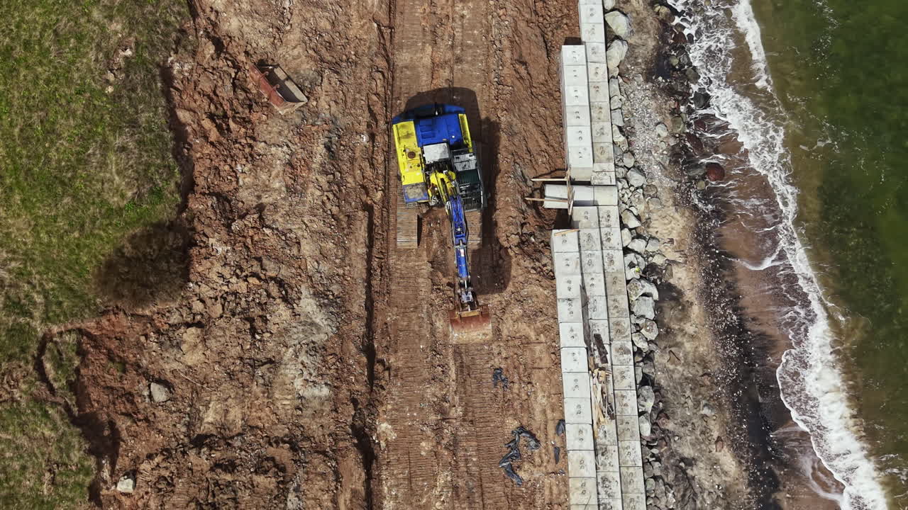 Construction work on a coastal area with heavy machinery moving earth near the water during daylight hours