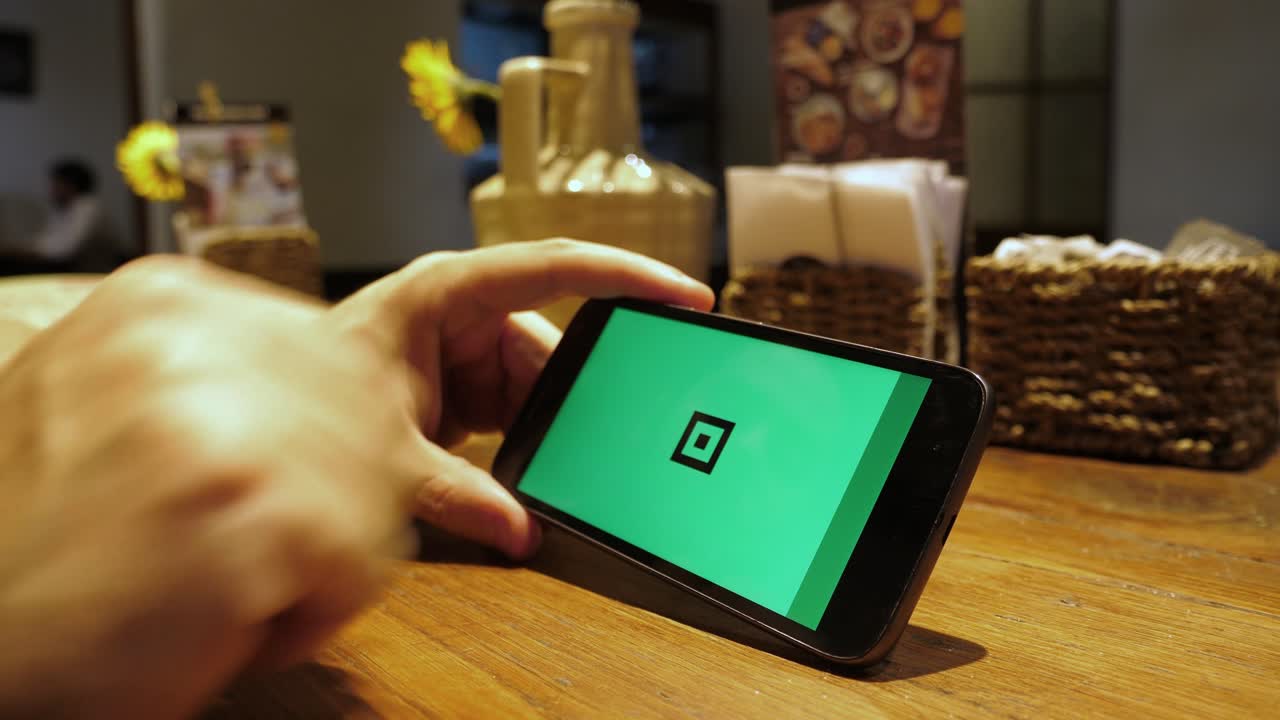 Person Tapping on Smartphone with Green Screen Display on Wooden Table