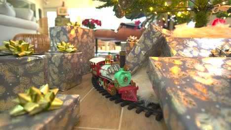 glide beneath a festive christmas tree, presents galore, showcasing a model train, spreading joy in a delightful wide forward sliding shot