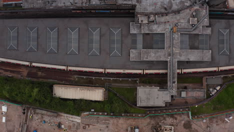 Aerial-birds-eye-overhead-top-down-ascending-footage-of-White-City-train-station.-Flat-roof-with-lightboxes.-London,-UK