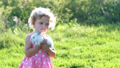 cute little girl holding a white bunny in a grassy field