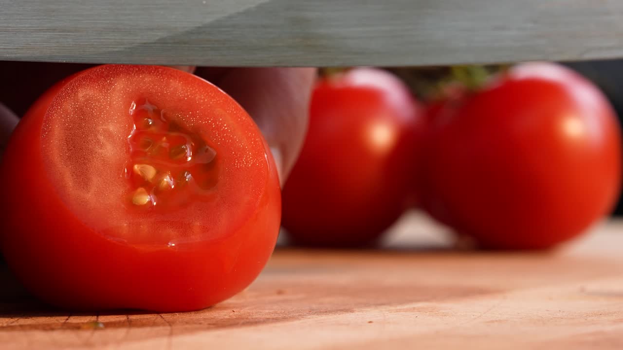 Slow-motion close-up in landscape format showing a tomato being sliced into ultra-thin pieces with an extremely sharp knife. The smooth blade motion highlights the texture and precision of the cut