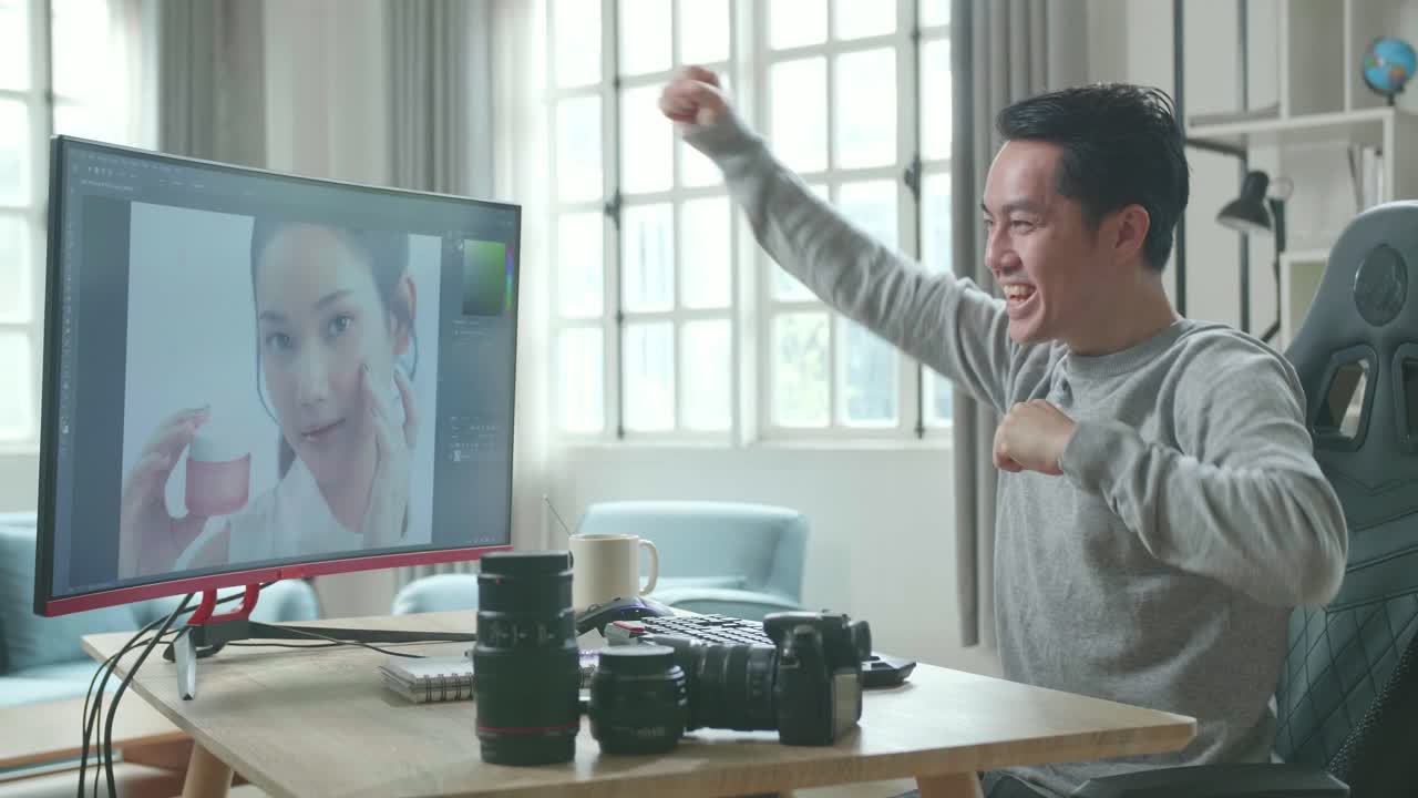 Asian Cameraman In Long Sleeved T-Shirt Being Happy Finishing Editing Photos By Desktop Computer While Working At Home