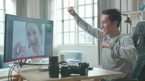asian cameraman in long sleeved t-shirt being happy finishing editing photos by desktop computer while working at home