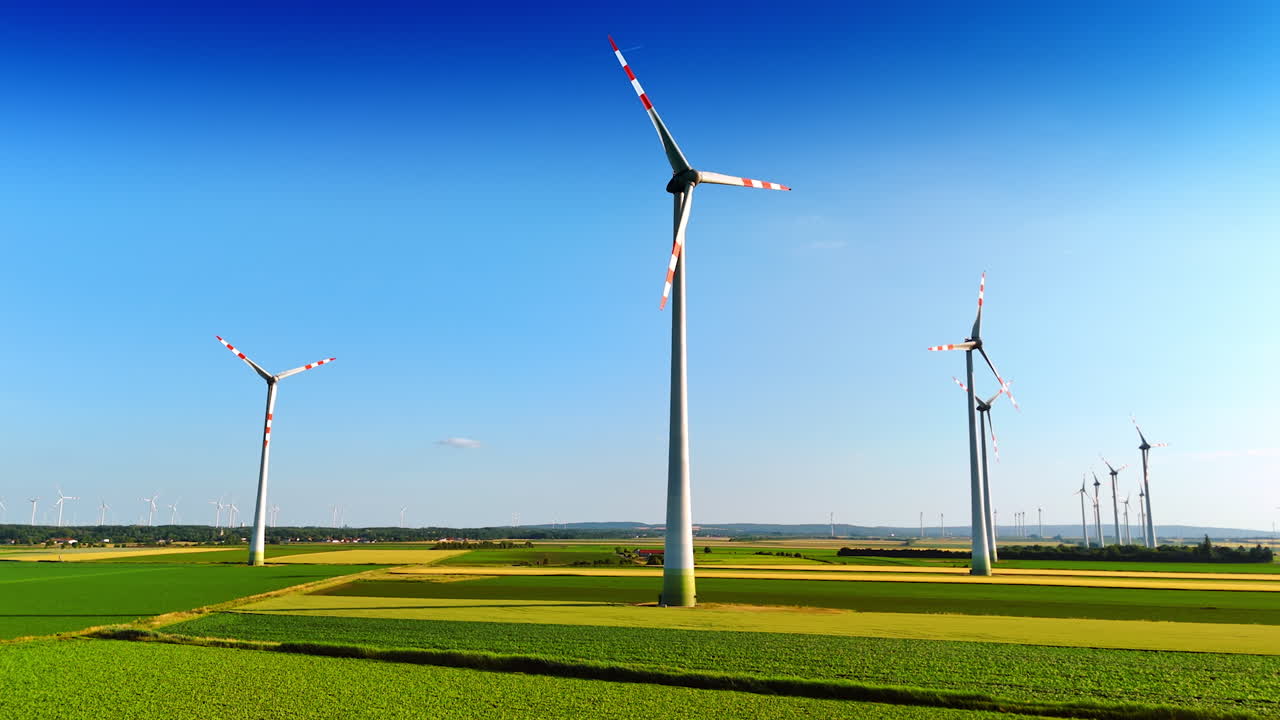 Green fields, blue clear skies and windmills rotating slowly. Production of green energy. Low angle view.