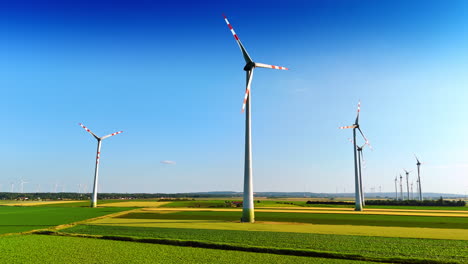 Green fields, blue clear skies and windmills rotating slowly. Production of green energy. Low angle view.