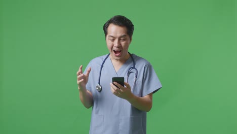 스마트폰을 사용하는 스테토스코프를 가진 아시아 남성 의사는 병원에서 녹색 화면 배경에 서서 와우라고 말합니다.