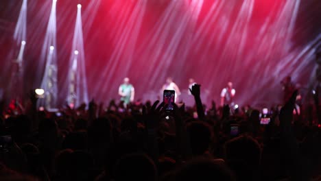 night rock concert with flashing lights stage, people cheer and clap their hands in unison