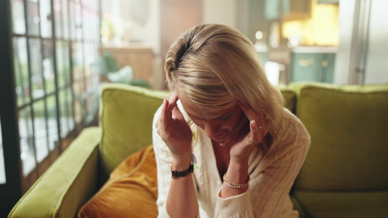 Distressed Woman Crying and Rubbing Temples on Sofa