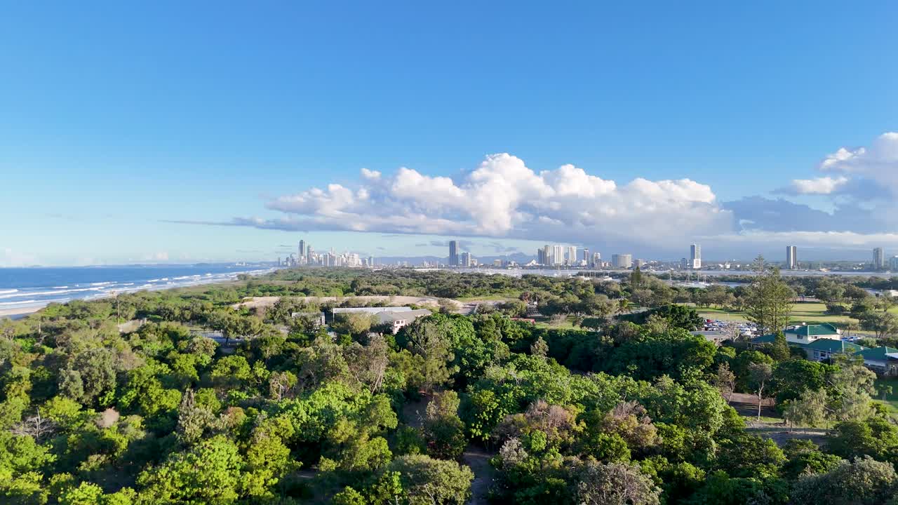 Drone footage captures expansive greenery and urban skyline under bright daylight in Gold Coast, Australia