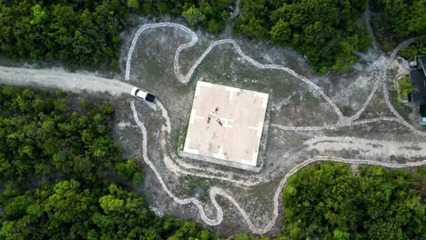 un avión no tripulado gira lentamente hacia abajo hacia un camión y tres personas acostadas en una plataforma de helicóptero en medio de un bosque tropical en las islas caimán en el caribe