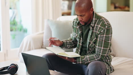 man working on laptop and writing in notebook at home