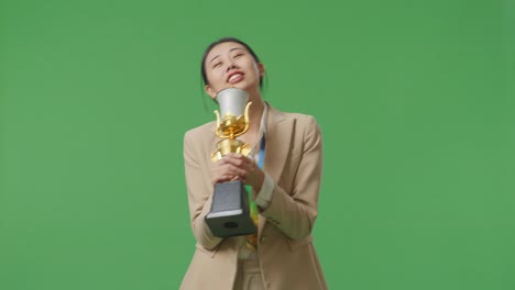 mujer de negocios asiática en traje con una medalla de oro cantando en un trofeo de oro celebrando la victoria como la primera ganadora en el fondo de la pantalla verde en el estudio
