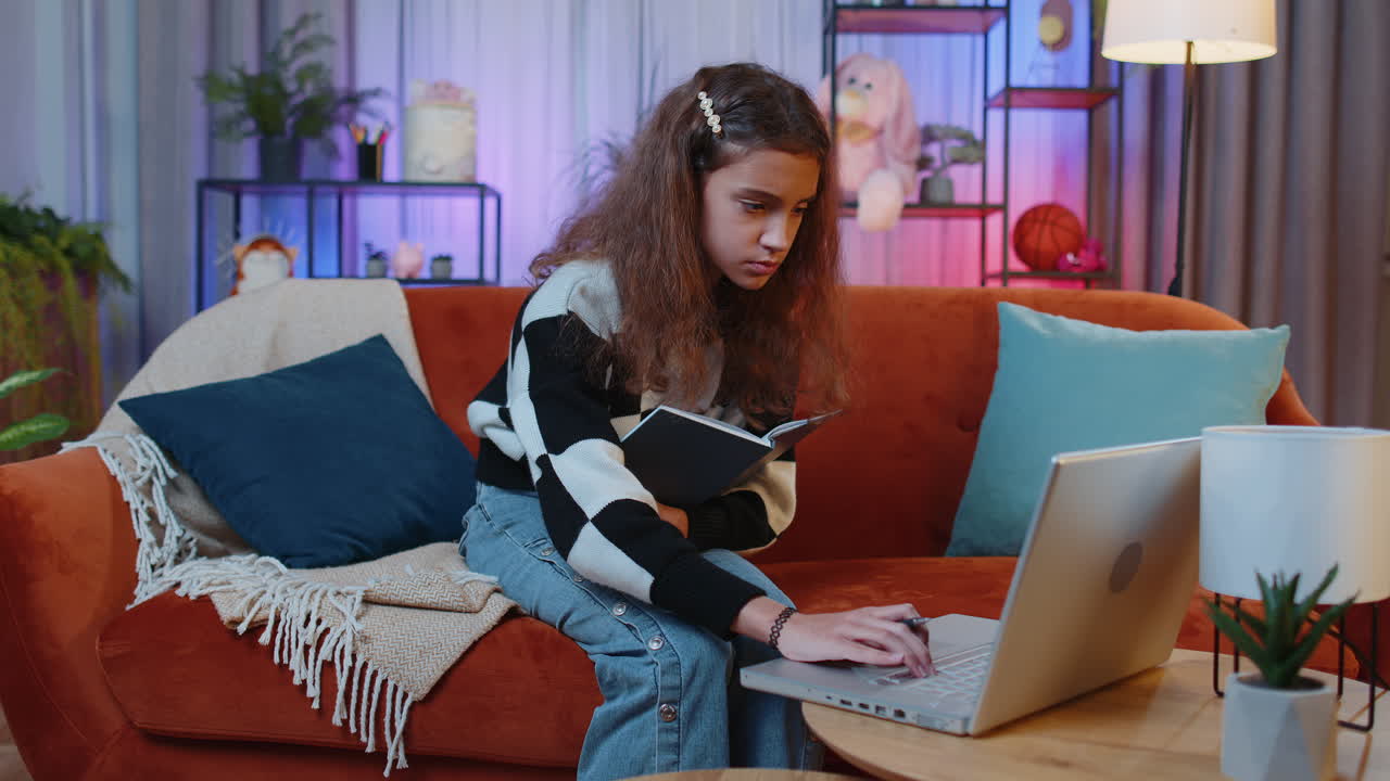 una joven está sentada en un sofá y trabajando en una computadora portátil. tiene un cuaderno en el regazo y está escribiendo en él. está centrada en su trabajo.