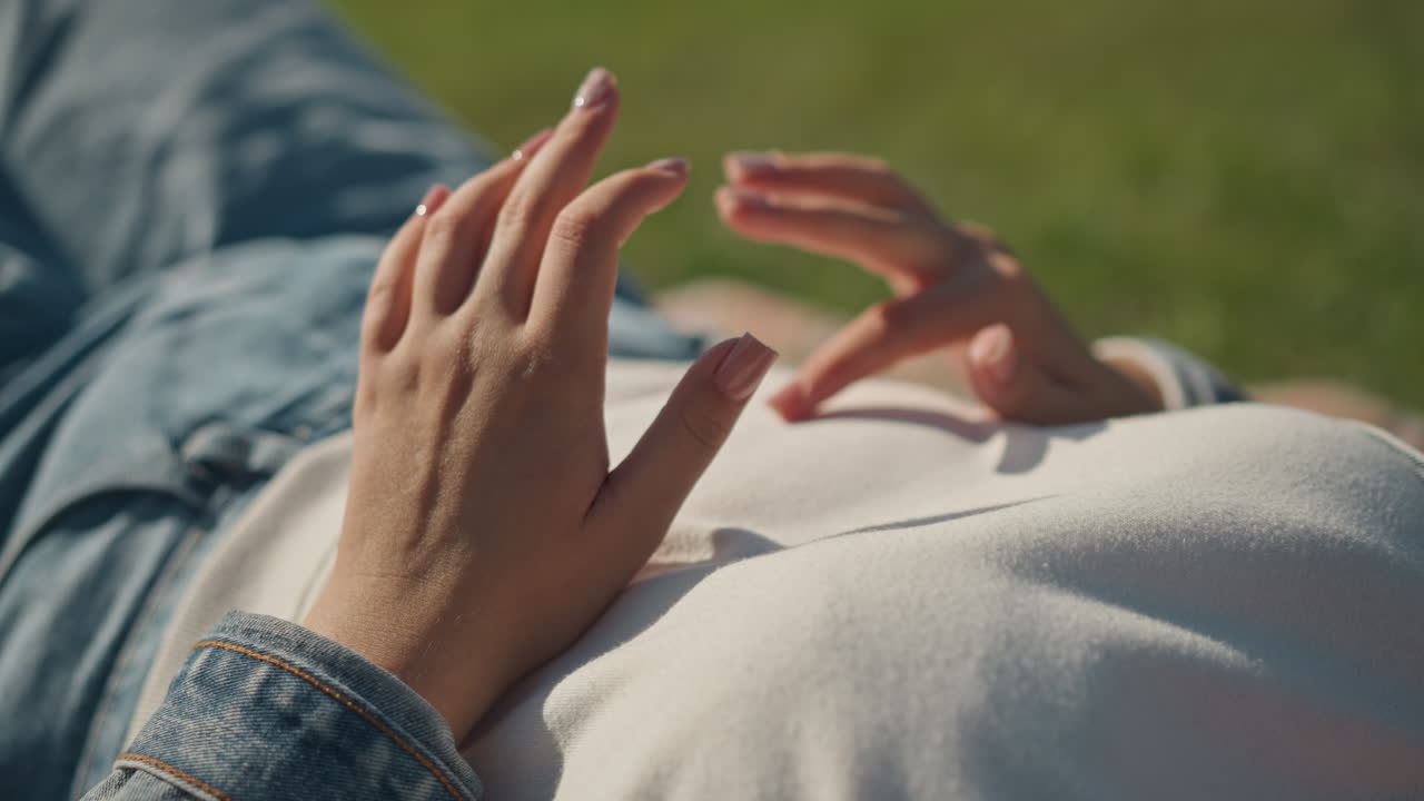 Gentle outdoor reflection. Peaceful woman gently touching her stomach under soft park lighting. An introspective woman lovingly tracing her belly with her fingers in tranquil outdoor setting