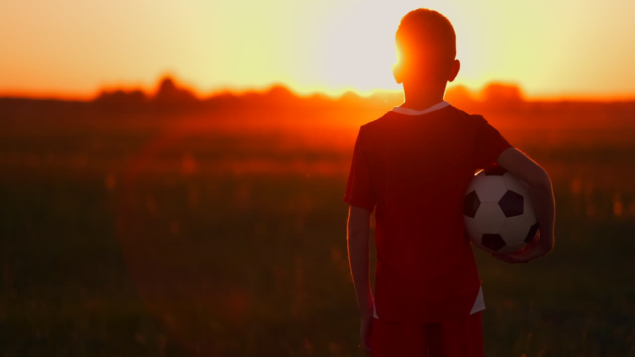 ragazzo con una palla in un campo al tramonto ragazzo sogna di diventare un giocatore di calcio ragazzo va in campo con la palla al tramonto.