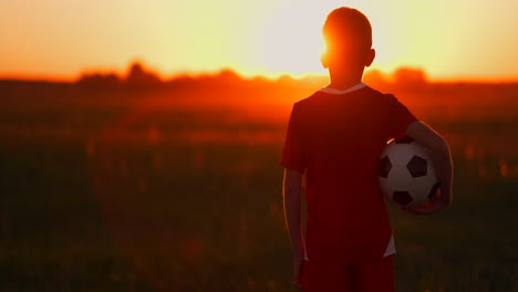 Junge-Mit-Einem-Ball-Auf-Einem-Feld-Bei-Sonnenuntergang.-Junge-Träumt-Davon,-Fußballspieler-Zu-Werden.-Junge-Geht-Bei-Sonnenuntergang-Mit-Dem-Ball-Auf-Das-Feld.