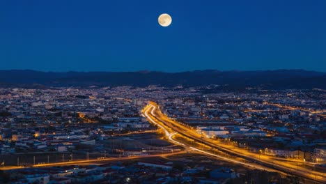 full moon over an illuminated city at night with light trails