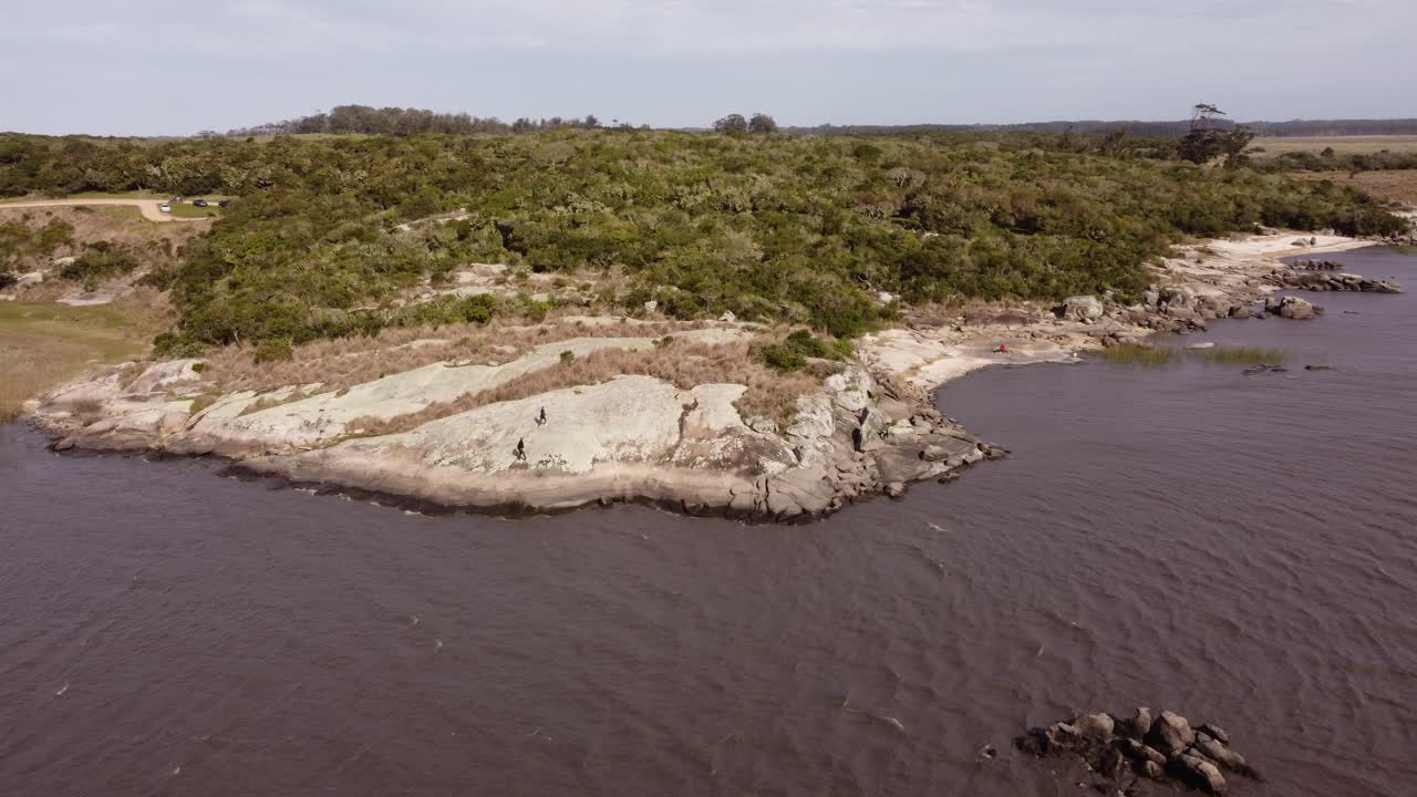 dos personas caminando sobre rocas a lo largo de la laguna negra, punta del diablo en uruguay