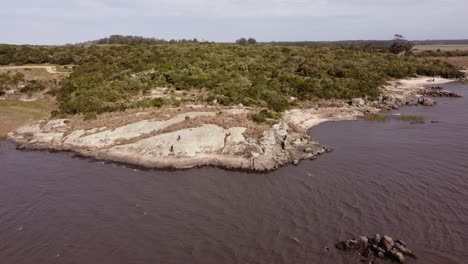 two people walking over rocks along black lagoon, punta del diablo in uruguay