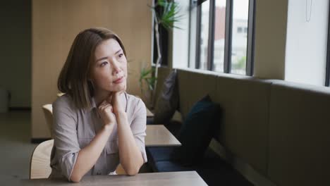 Asian-businesswoman-sitting-looking-out-of-window-in-modern-office