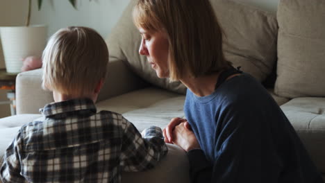 young boy and mother reading a book while sitting next to the sofa