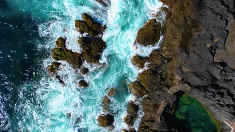 top-down view of calm ocean waves with turquoise water splashing on the rocky shore line