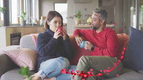 Animación-De-Corazones-Sobre-Parejas-Diversas-Sentadas-En-Un-Sofá-Y-Tomando-Café-En-Casa